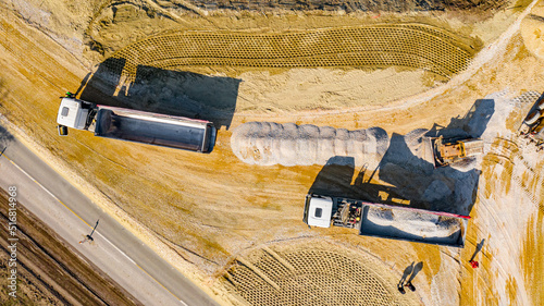 Top view on tipper truck as unloading gravel from a trailer while another is waiting to be unloaded, bulldozer flatting construction site photo