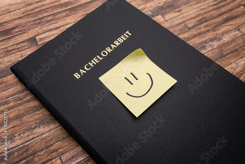 Adhesive note with a smiley on a Bachelorarbeit (bachelor thesis). Printed and bound thesis with a black cover. Finishing studies in Germany and becoming a graduate student. photo