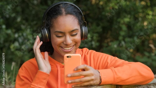 Beautiful mixed race African American girl teenager young woman listening to music on her smartphone or cell phone wearing wireless headphones and drinking take out coffee