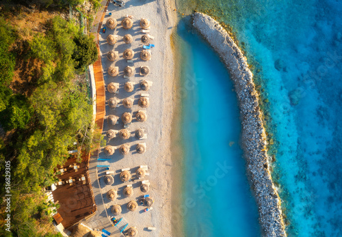 Fototapeta Naklejka Na Ścianę i Meble -  Aerial view of sandy beach with umbrellas, sea, green trees, breakwater at sunset in summer. Blue lagoon in Oludeniz, Turkey. Tropical landscape with sea bay, transparent water. Top view from drone