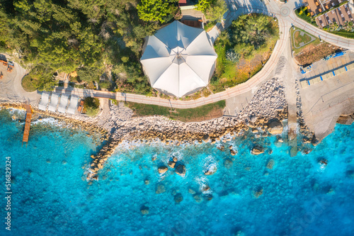 Fototapeta Naklejka Na Ścianę i Meble -  Aerial view of sandy beach with umbrellas, green trees at sunset in summer. Blue lagoon in Oludeniz, Turkey. Tropical landscape with sea bay, transparent blue water. Top view from drone. Nature