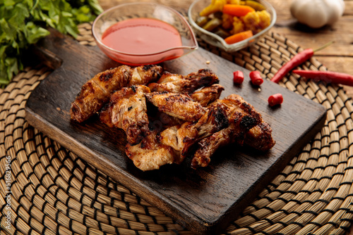 GRILLED CHICKEN WINGS with sauce and pickle served in a wooden cutting board isolated on wooden table background side view of appetizer