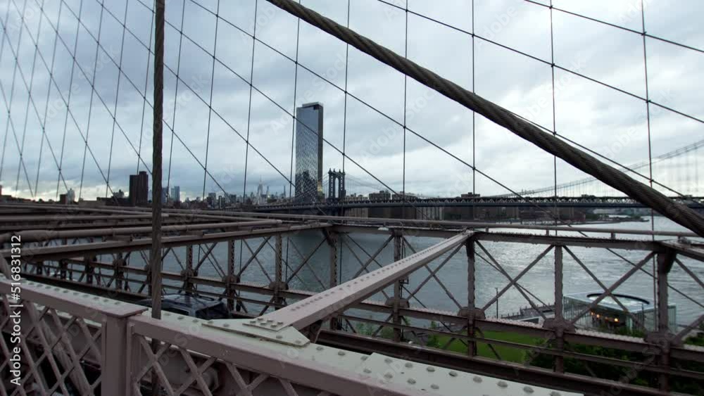 Walking along the Brooklyn Bridge, view of the road with driving cars, East river and New York cityscape with high skyscrapers under the grey sky. USA Walking along the Brooklyn Bridge, view of the road with driving cars, East river and New York cityscape with high skyscrapers under the grey sky. USA