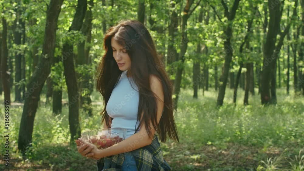 happy woman enjoying eating ripe strawberries while standing in the forest during family vacation. happy woman enjoying eating ripe strawberries while standing in the forest during family vacation.