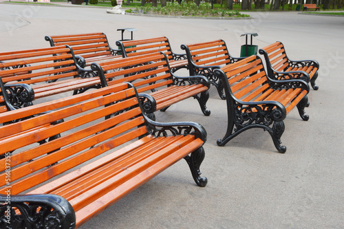 Lots of wooden benches in one place. Brown benches with black cast-iron sidewalls stand on the street in a city park. photo