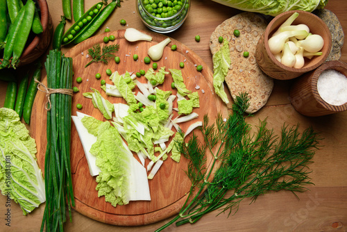vegetables on a wooden kitchen board, green onions, dill and peas, sliced cabbage on a wood background, concept of fresh and healthy food, still life