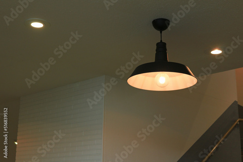 Illumination of an iron pendant lamp shade with a simple design hung in a dimly lit room