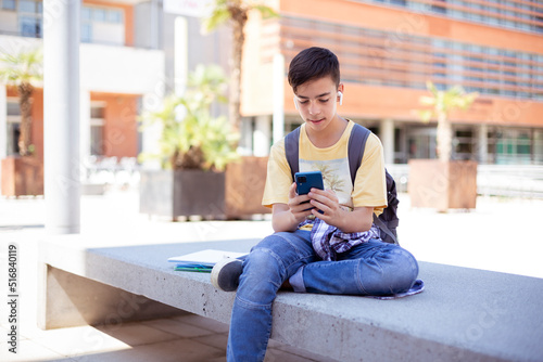 Caucasian teenage student boy using a smart phone outdoors. Space for text.
