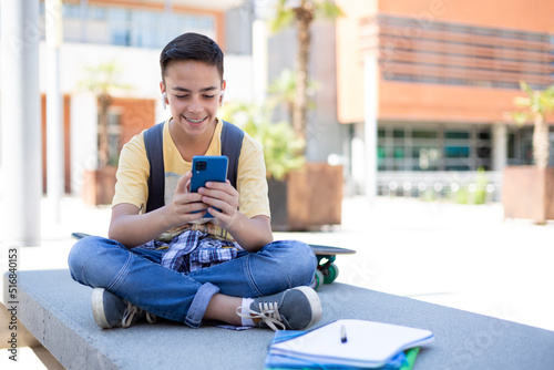 Smiling high school student boy using mobile phone outdoors. Space for text.