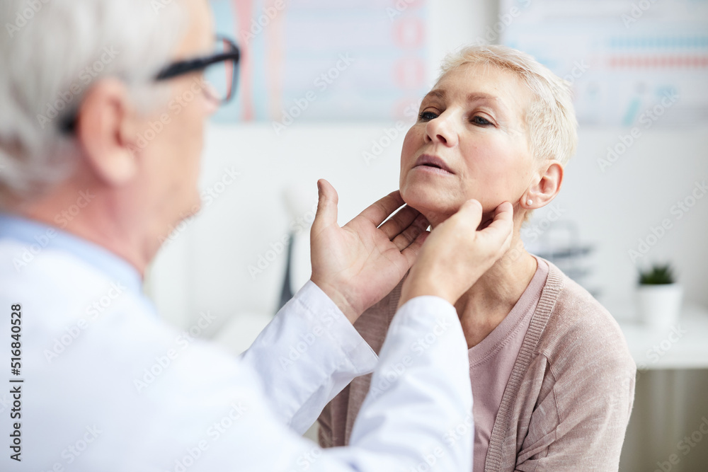 Over shoulder view of qualified cancer doctor touching neck of mature patient while checking size of lymph nodes Over shoulder view of qualified cancer doctor touching neck of mature patient while checking size of lymph nodes