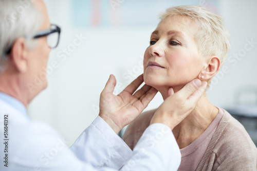 Over shoulder view of senior endocrinologist touching neck of mature female patient while examining her thyroid