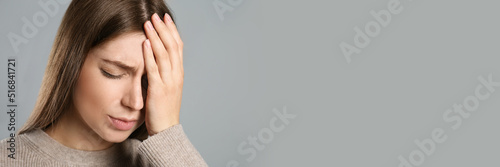 Young woman suffering from migraine on grey background, space for text. Banner design photo