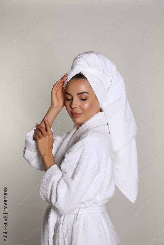 Beautiful young woman wearing bathrobe and towel on head against light background Beautiful young woman wearing bathrobe and towel on head against light background