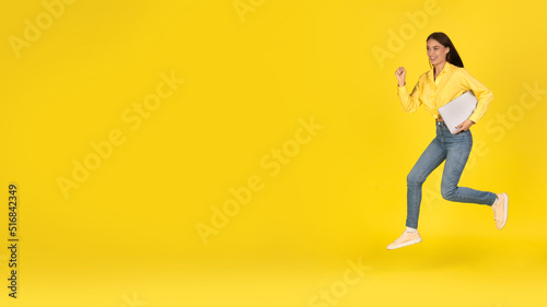 Happy Woman Running Holding Laptop Looking Aside Over Yellow Background © Prostock-studio