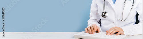 Doctor typing on computer keyboard in office. Physician in uniform uses computer at desk. Professional diagnosis and treatment tele medicine. Professional healthcare wide banner