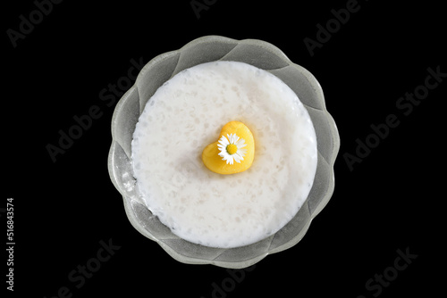 Homemade tapioca pudding with coconut milk, decorated with fresh nectarine in a shape of heart and edible daisy flower. Isolated on black background. Romantic concept, inspiration