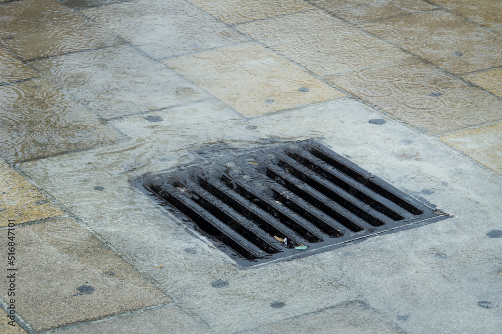 Water during a rainstorm flows into the drainage grate. Rainwater flowing down the impervious pavement to the storm drain equipped with cast iron grid during a rain. Water during a rainstorm flows into the drainage grate. Rainwater flowing down the impervious pavement to the storm drain equipped with cast iron grid during a rain.