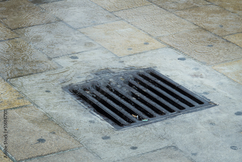 Water during a rainstorm flows into the drainage grate. Rainwater flowing down the impervious pavement to the storm drain equipped with cast iron grid during a rain. photo