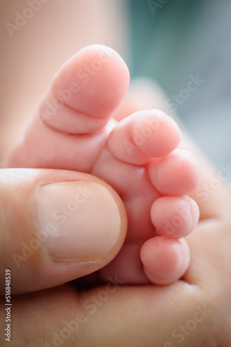 Close-up detail of mother holding cute and soft baby small leg in her hands. Macro abstract view of sweet baby foot fingers. Soft child skin feet. Love and family emotion