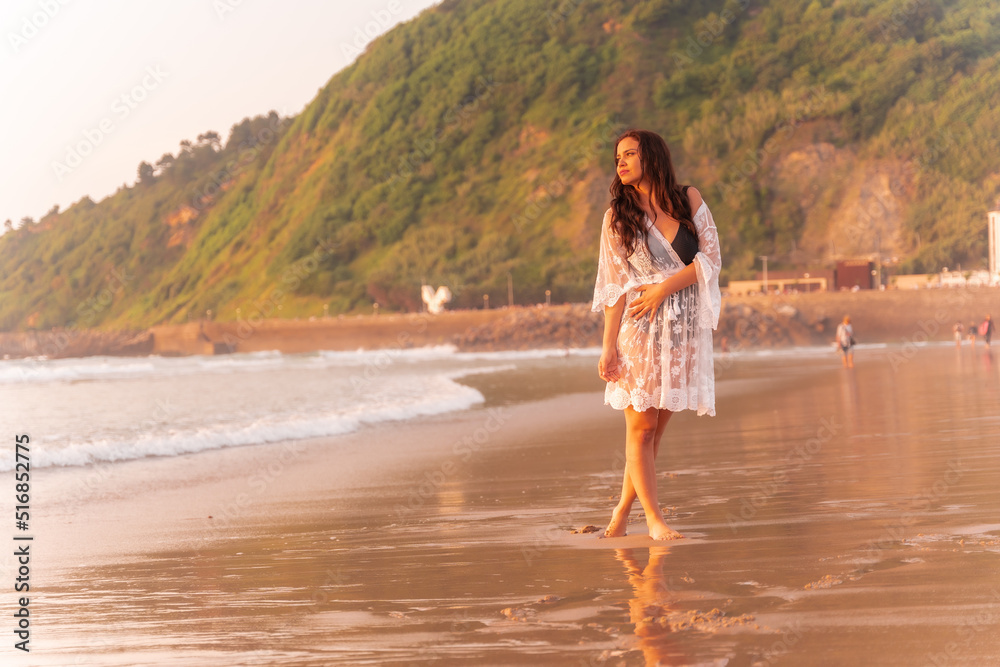 Portrait of a woman at sunset in a white dress enjoying vacations on the beach