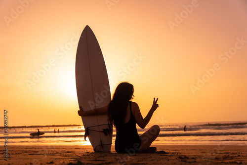 Silhouette of a surfer woman on a beach at sunset making the peace symbol