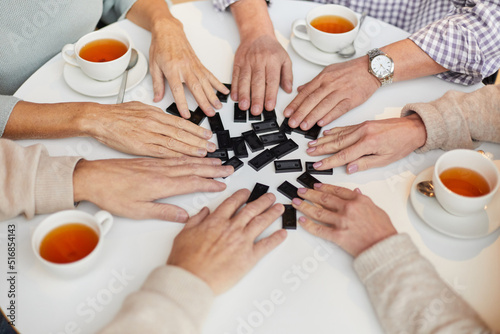 Close-up of unrecognizable senior people sitting at table with tea cups and mixing domino pieces while preparing to play dominoes
