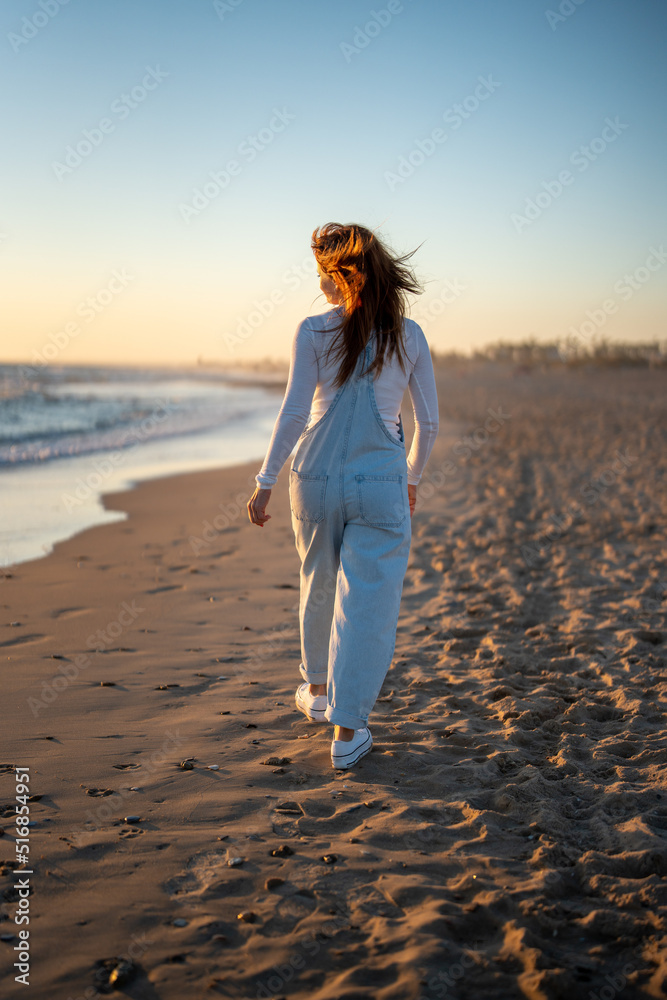 red-haired woman walking on the beach while looking at the sea