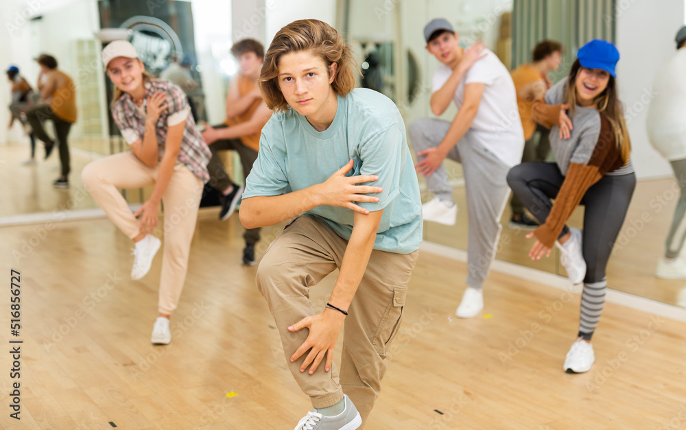Portrait of cheerful teenage boy practicing hip-hop movements during group dance lesson in studio.