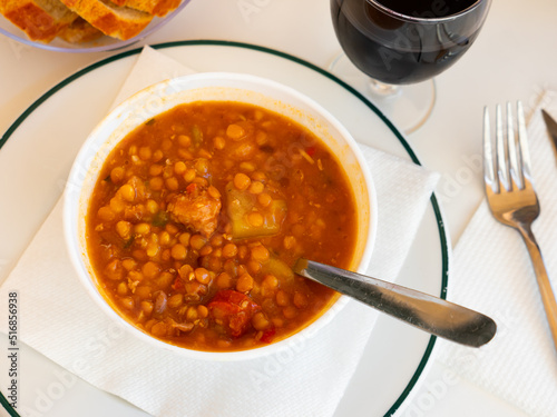 Spicy stewed lentils with suasage and vegetables with thick tomato sauce served in white plate. Typical Spanish cuisine