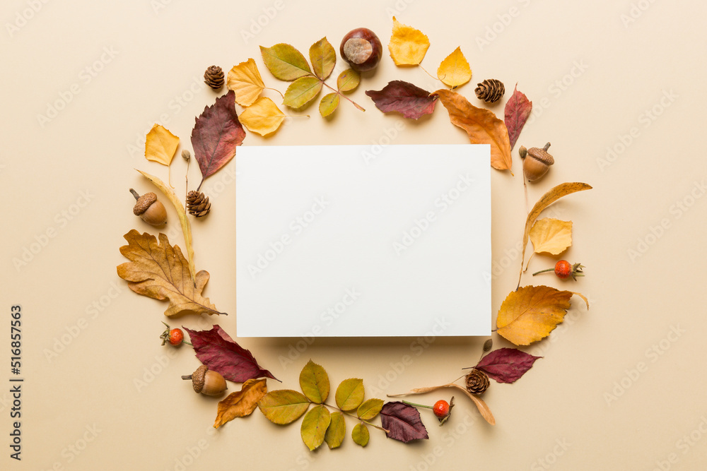 Fototapeta premium Autumn composition with paper blank and dried leaves on table. Flat lay, top view, copy space