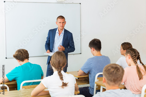 Young students sitting in classroom and listening to male teacher.
