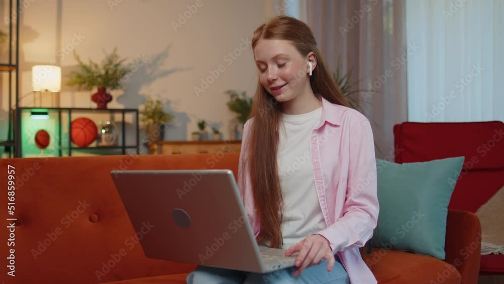 Stockvideo Young teen child girl sitting on couch, looking at laptop, making video webcam conference call with friends or family, enjoying pleasant conversation. Ginger kid laughing, waving hello alone in home | Adobe Stock
