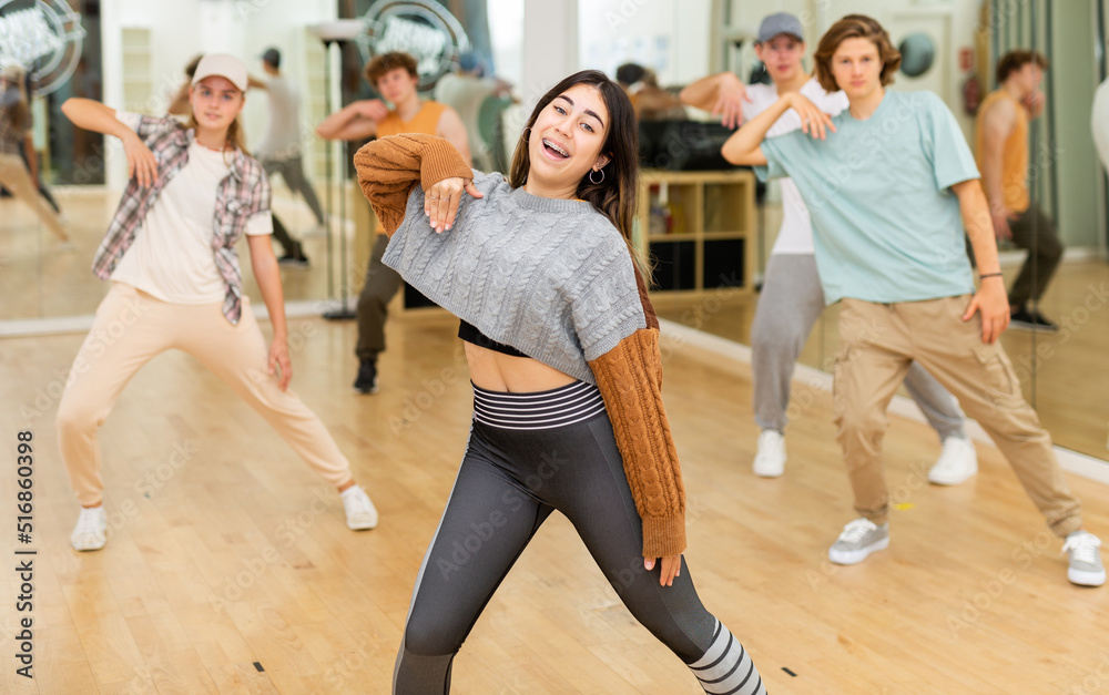 Portrait of expressive teen girl krump dancer in choreographic studio with dancing teenagers in background.