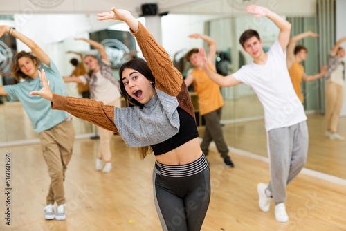 Cheerful emotional teen girl enjoying while training movements of modern group dance in choreography class .