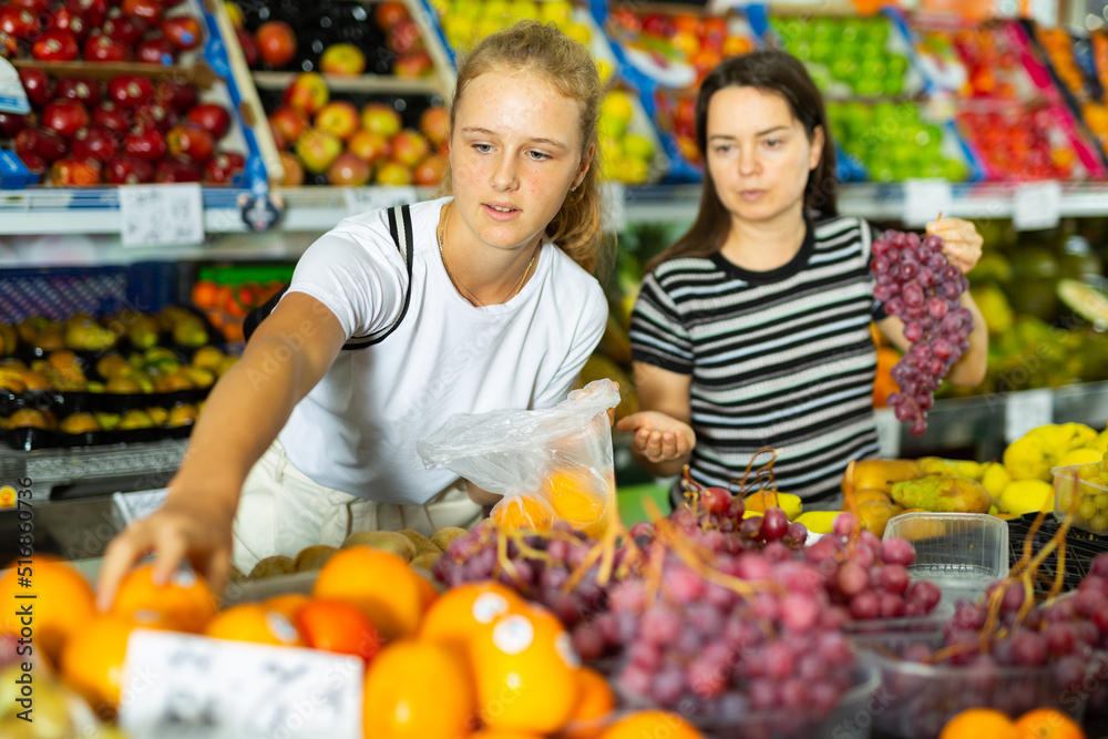 Portrait of teenage girl and her mother who buying fresh red grape at grocery shop