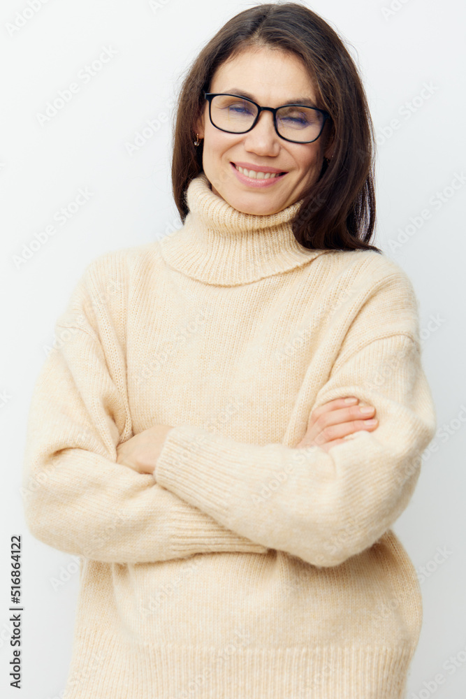Fototapeta premium A sweet, beautiful, intelligent woman in a stylish beige sweater, stands with glasses for vision with her arms crossed on her chest