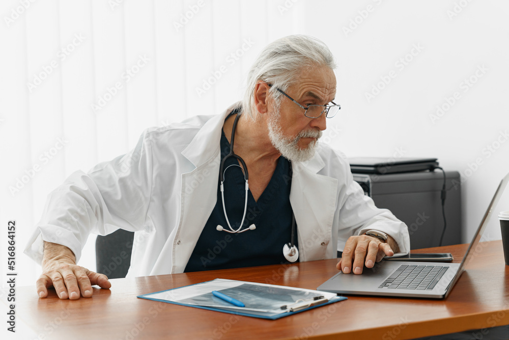 Senior healthcare worker doing some paperwork and using laptop while working at doctor's office Senior healthcare worker doing some paperwork and using laptop while working at doctor's office
