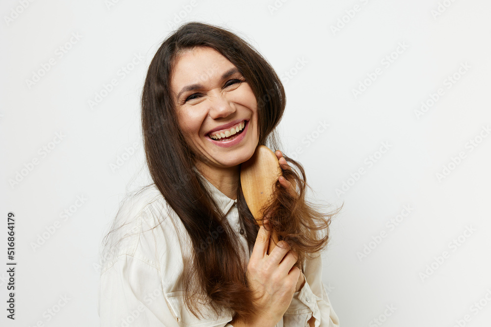 portrait of a beautiful woman joyfully combing her healthy long dark hair with a wooden comb smiling broadly with even bright teeth. Photo on a light background portrait of a beautiful woman joyfully combing her healthy long dark hair with a wooden comb smiling broadly with even bright teeth. Photo on a light background