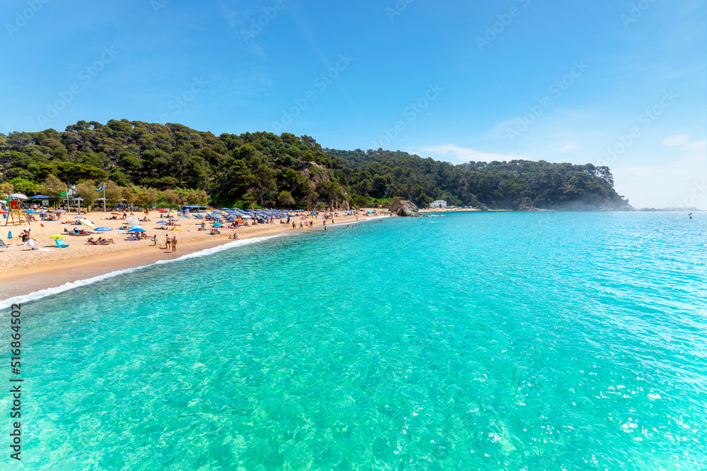 View from the clear turquoise sea as the fog breaks at morning along the Cala Santa Cristina sandy beach on the Costa Brava coast in Lloret de Mar, Spain.