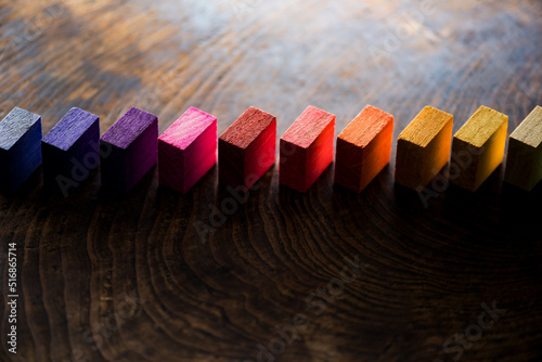 Colored wooden blocks aligned on old vintage wooden table, with light coming through and dark shadows. For something with concept of variations or diversity. Shallow depth of field.
