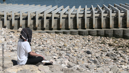Young male doing meditation on a stone beach on industrial background