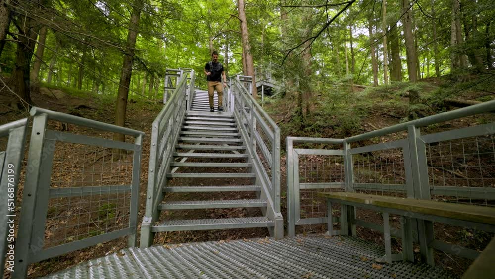 Male hiker with backpack quickly descends steep metal staircase in forest landscape, walking towards camera static low angle Male hiker with backpack quickly descends steep metal staircase in forest landscape, walking towards camera static low angle