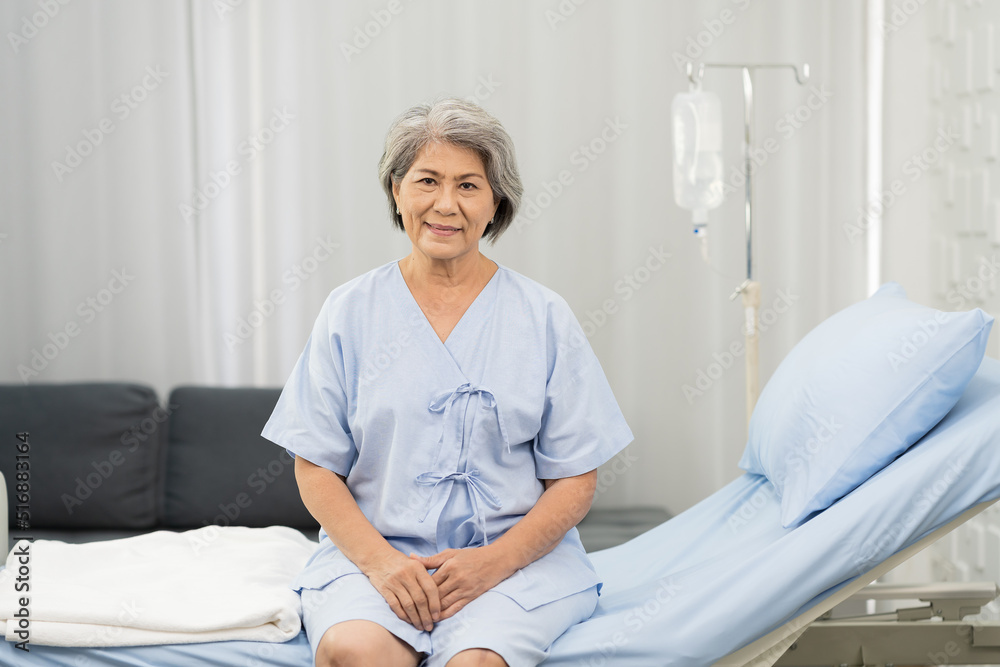 Fototapeta premium Senior asian woman sitting on bed with receiving saline solution from bag at hospital ward. medicine, health care, old people and quarantine concept