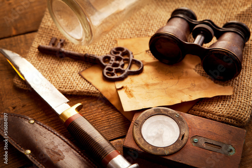 Treasure hunting setting, A compass, binoculars, knife and an old key on an old wooden desk