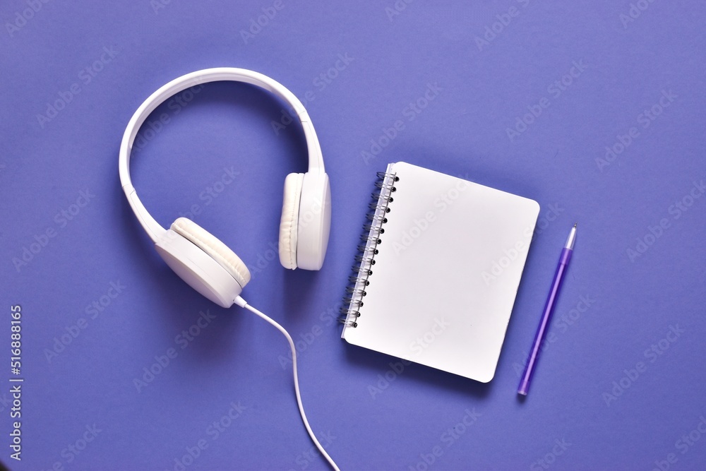 Headphones with blank notepad and pen on very peri violet background. Flat lay composition with copy space Headphones with blank notepad and pen on very peri violet background. Flat lay composition with copy space