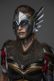 Portrait of woman amazon with brown hairs from past dressed in dark armor isolated on gray background.