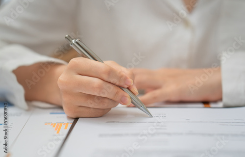 hand of woman holding pen with writing on paper report in office.