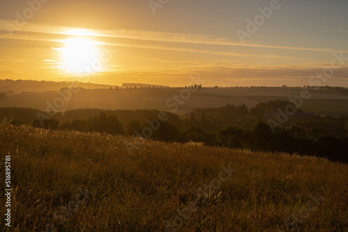 Spectacular sunrise in the rolling hill landscape in the south of Limburg with a view on the meadows and on a row of poplar trees  creating the feeling of being in the Siena Province of Italy.