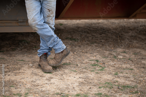 crossed legs of man standing wearing dirty jeans and work boots photo