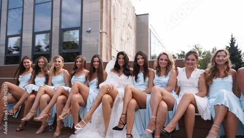 Attractive bride and bridesmaids switching crossing legs sitting on bench seductively in provocative way. Pretty women in identical dresses cross legs simultaneously together flirting at camera.